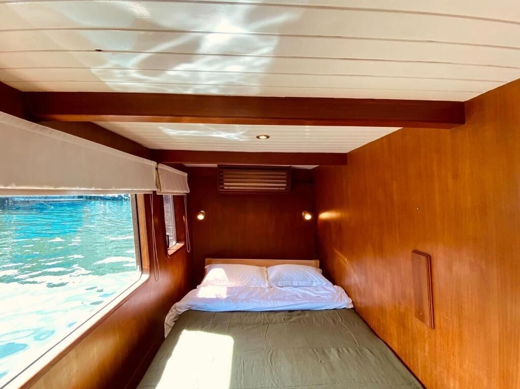 Una cabaña pequeña con una cama, un ventanal con vista al agua y techo de madera.