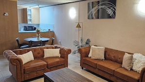 Una sala de estar con dos sofás de cuero marrón, una mesa de centro y un comedor con una mesa y sillas.