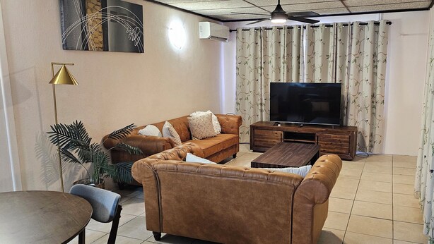 Una sala de estar con un sofá marrón, una mesa de centro, un televisor y un ventilador de techo.
