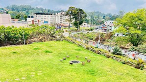 A grassy area with a few trees and a building in the background. - Caron Niron Two Bedroom Villa (Kodaikanal)