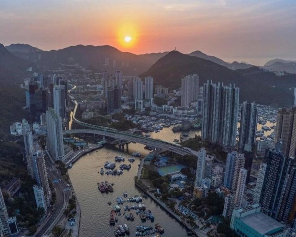 Une vue urbaine avec des gratte-ciel, une rivière et un pont, le tout baigné par les couleurs du coucher de soleil.