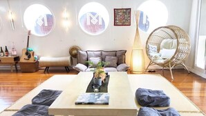 Una habitación con un sofá, una silla redonda de mimbre, una mesa con cojines y una guitarra.