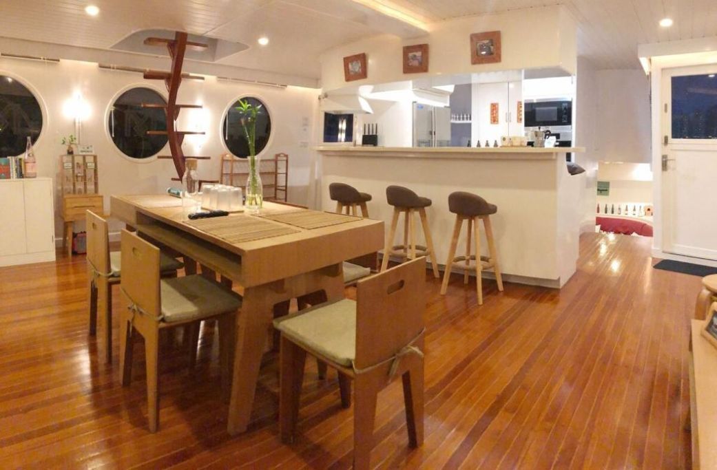 Un comedor con una mesa y sillas de madera, una cocina al fondo y vistas de la ciudad por la noche.