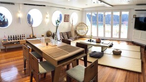 Una habitación con piso de madera, una mesa de comedor con sillas, un sofá, un televisor y ventanas grandes.