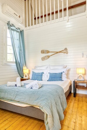 A bedroom with a bed, a wooden floor, a window with curtains, and a wall-mounted paddleboard. - Fleur de Sel - Villa 4 Piscine L'etang-sale (La Celle-sous-Gouzon)