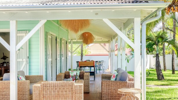 A covered outdoor area with wicker furniture, a pool, and a view of a house with a blue exterior.