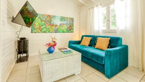 A room with a teal sofa, a white coffee table with books, a colorful painting, and a window with curtains.
