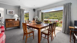 Ein Essbereich mit Holztisch und -stühlen, einer Couch, einem Schrank und Blick auf eine grüne Landschaft durch große Fenster.