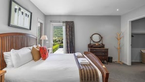 Ein Schlafzimmer mit Bett, Nachttisch, Kommode und Spiegel, mit Blick ins Freie.