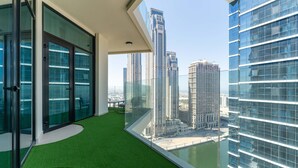 A modern balcony with glass doors, a green artificial turf floor, and a view of high-rise buildings.