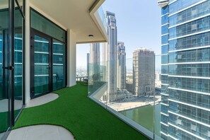 A modern balcony with glass doors, a green artificial turf floor, and a view of high-rise buildings.