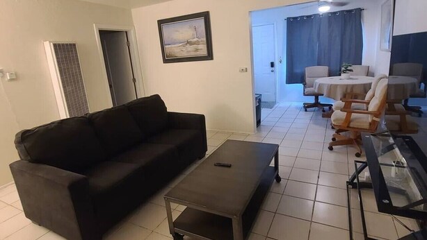 Ett vardagsrum med en svart soffa, ett litet bord och ett soffbord i glas. Längre bak i rummet finns en matplats med ett bord och stolar.