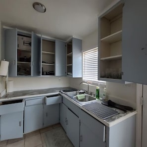 Una cocina compacta con armarios empotrados, un lavamanos y una ventana con persianas.