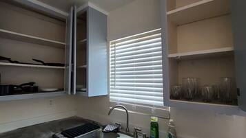 A kitchen with a built-in sink, a window with blinds, and open cabinets.