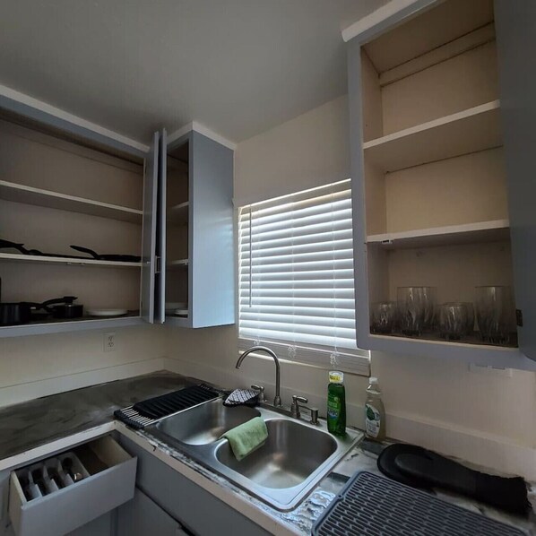 A kitchen with a built-in sink, a window with blinds, and open cabinets.