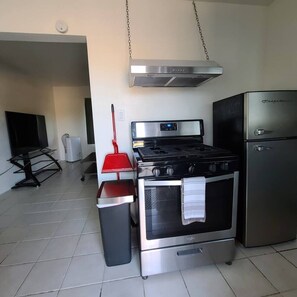 A kitchen with a stove, oven, and refrigerator, a TV, and a red mop.