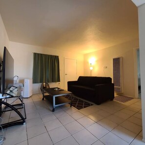 A living room with a sofa, a coffee table, a TV, and a window with curtains.