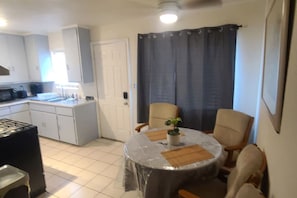 A compact kitchen with white cabinets, a black countertop, and a dining area with a round table and two chairs.