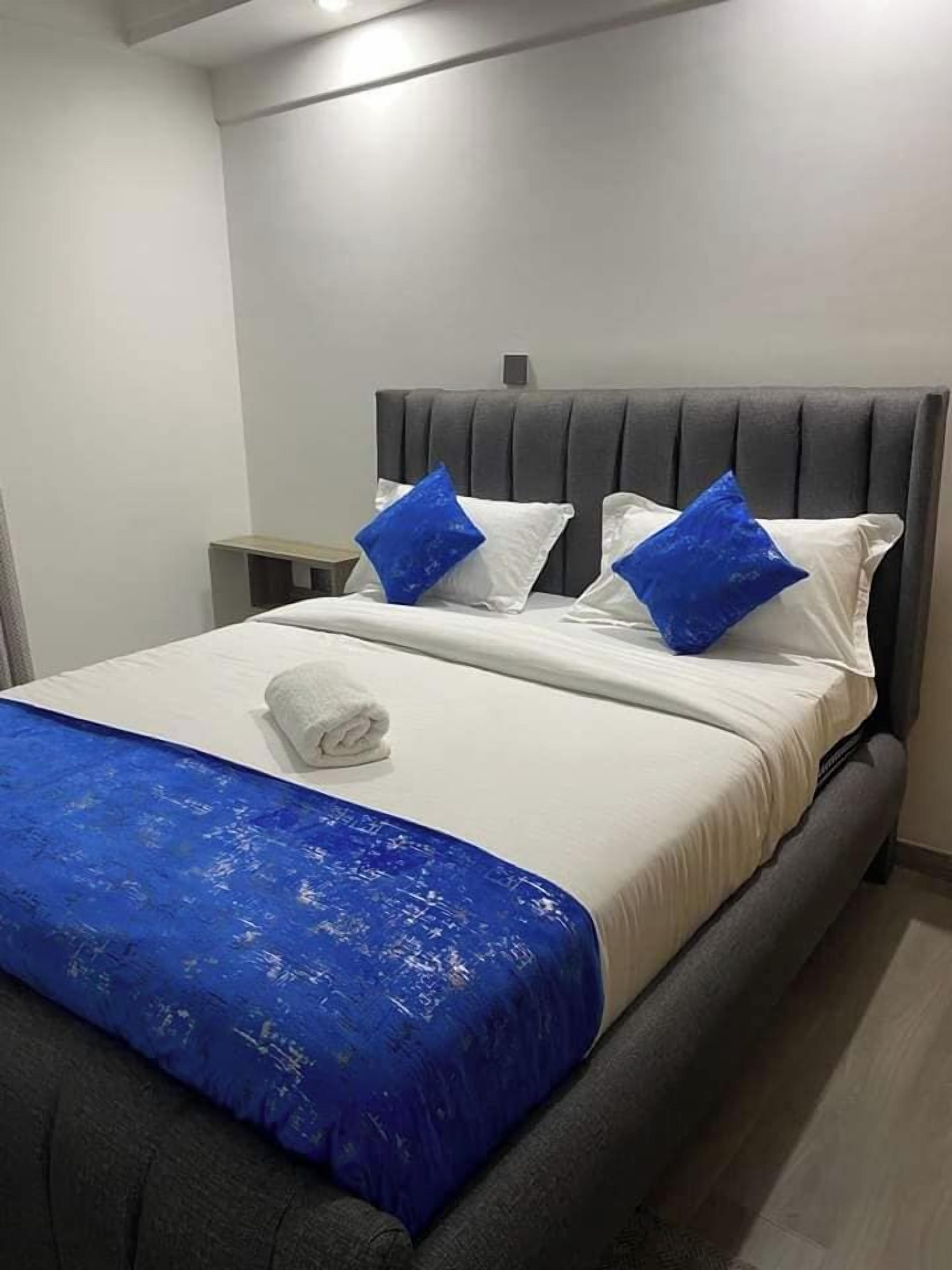 Une chambre d’hôtel avec un lit, une table de chevet et un plaid bleu.