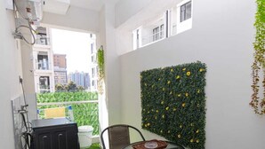 A small balcony with artificial grass, two wicker chairs, a glass table, and a wall-mounted flower display. - Kilimani Homes (Nairobi)
