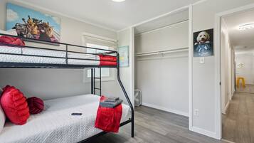 A bunk bed room with a painting of dogs on the wall, a small heater, and a door leading to another room.