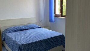 Un dormitorio con cama, mesita de noche, ventana con cortinas azules y un enchufe.