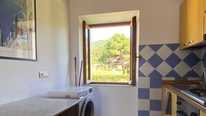 A compact kitchen with a built-in washing machine, a window with a view of greenery, and a tiled backsplash.