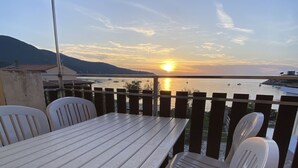 A balcony with a table and chairs overlooking a body of water at sunset.