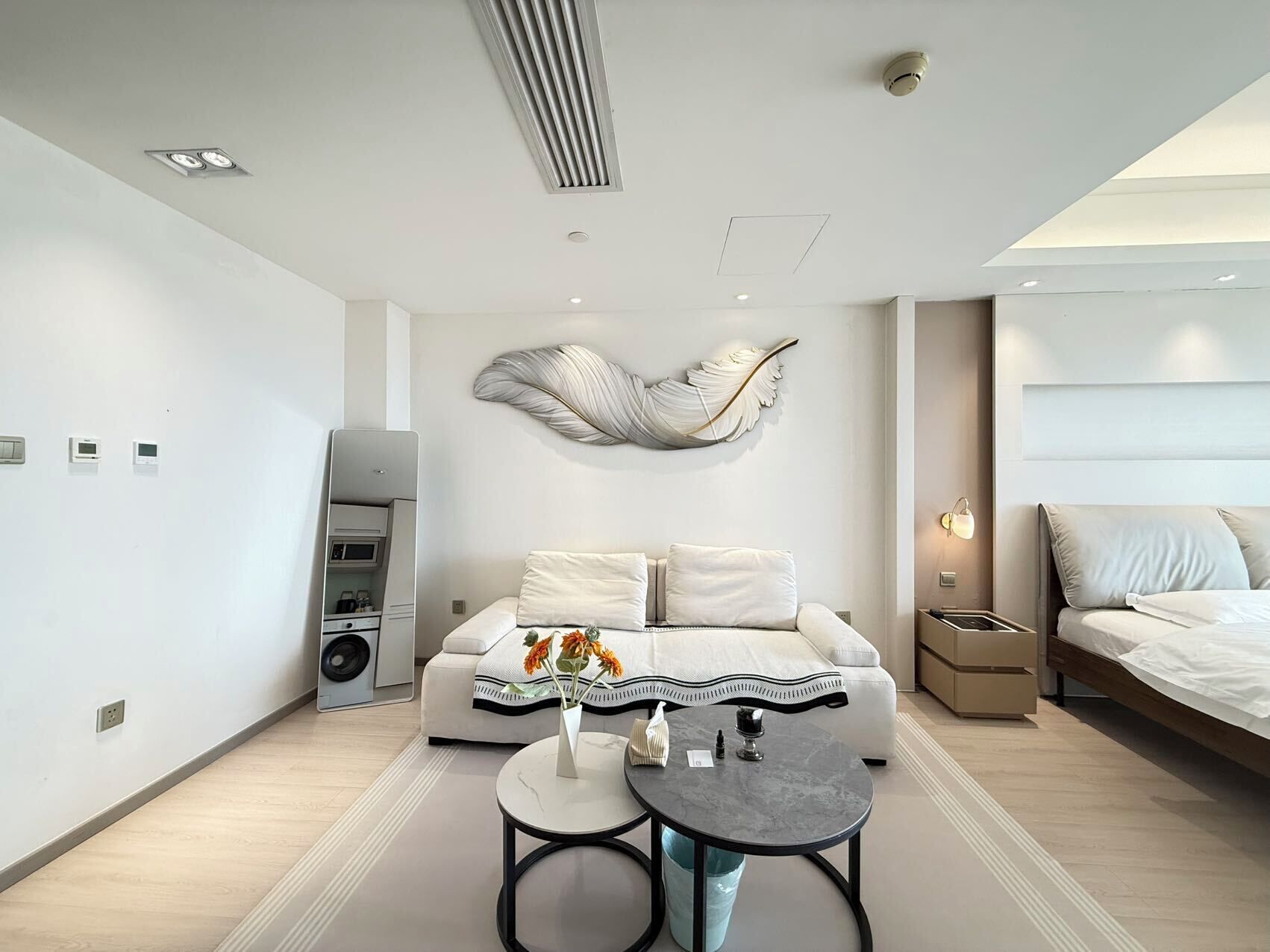 Een moderne hotelkamer met een bank, een klein rond tafeltje, een decoratief wandobject, een bed en een ingebouwde speaker.