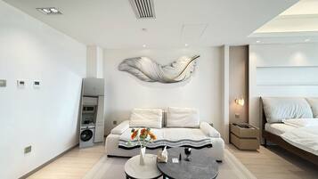 Een moderne hotelkamer met een bank, een klein rond tafeltje, een decoratief wandobject, een bed en een ingebouwde speaker.