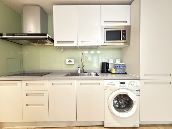 A compact kitchen with a washing machine, a microwave, a sink, and a coffee maker. - Yoki shimao international apartment (Beijing)