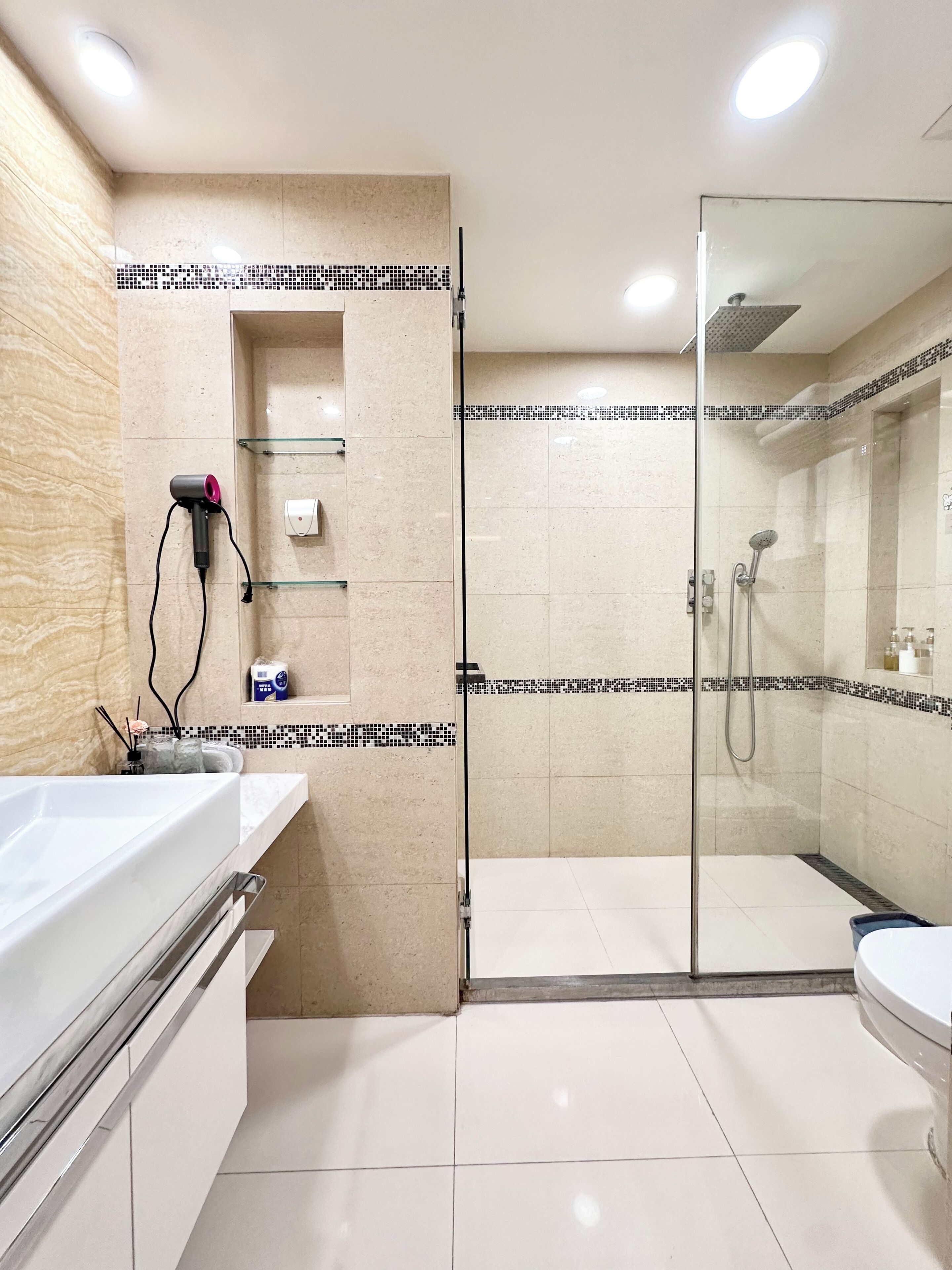 A modern bathroom with a glass shower enclosure, a white sink, and a hairdryer on the wall.