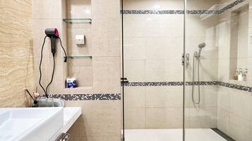 A modern bathroom with a glass shower enclosure, a white sink, and a hairdryer on the wall.