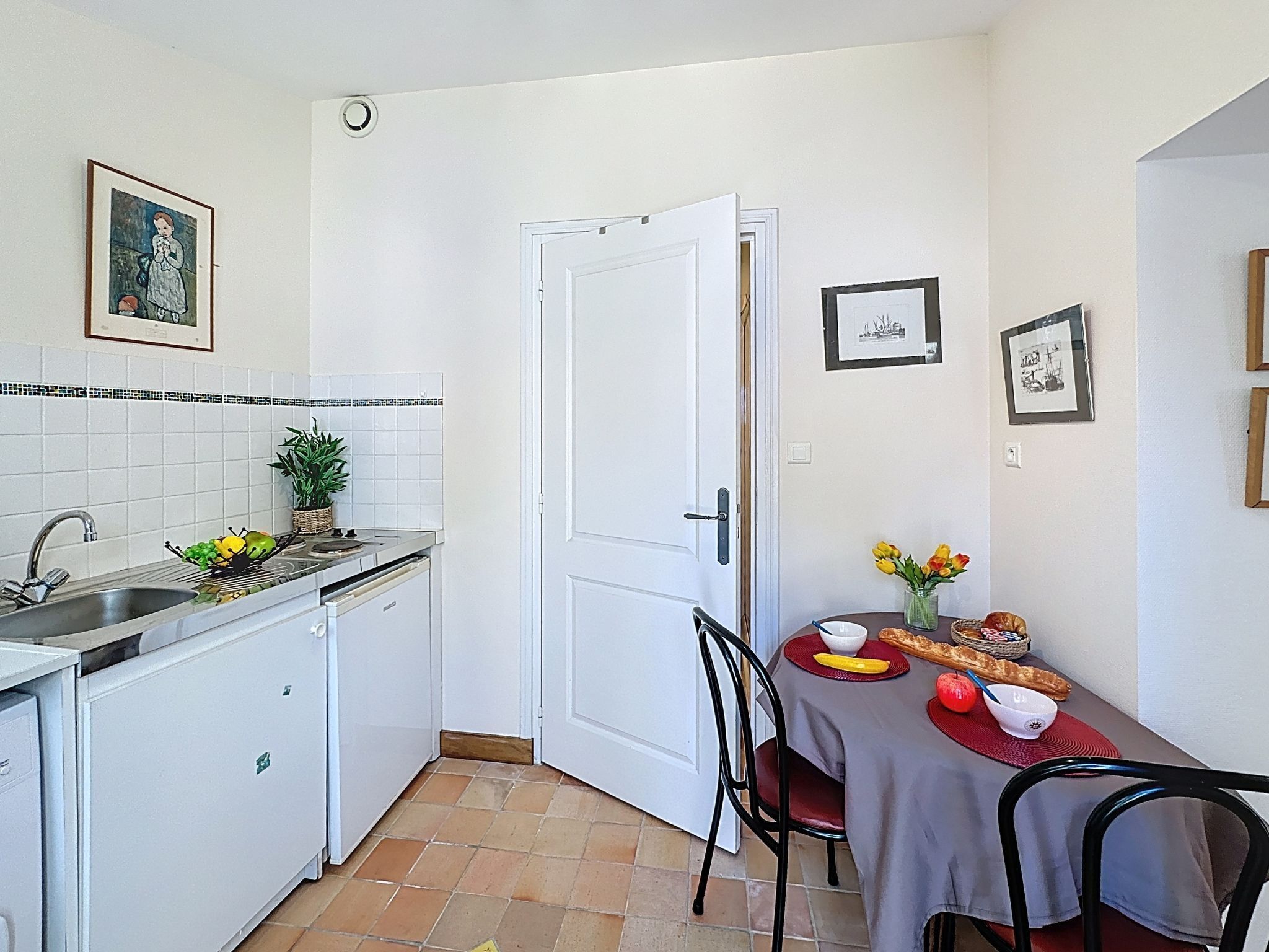 A compact kitchen with a sink, stove, and white cabinets. A dining table with chairs is positioned near a white door.