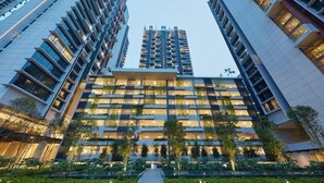 Een modern, meerhoog gebouw met een centraal atrium, omringd door groen en nabij hoogbouw.
