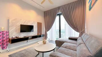 A modern living room with a flat-screen TV, a sofa, a coffee table, and a large window with curtains.