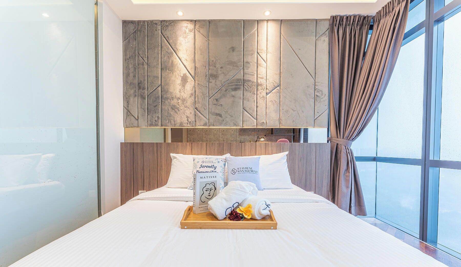 Moderni hotellihuone, jossa on suuri sänky, puinen pääty, marmoriseinä ja näkymä suurista ikkunoista.