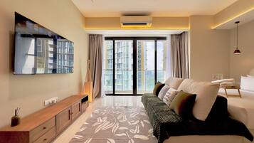 A modern hotel room with a large bed, a sofa, a TV mounted on the wall, and a view of the city through the windows.