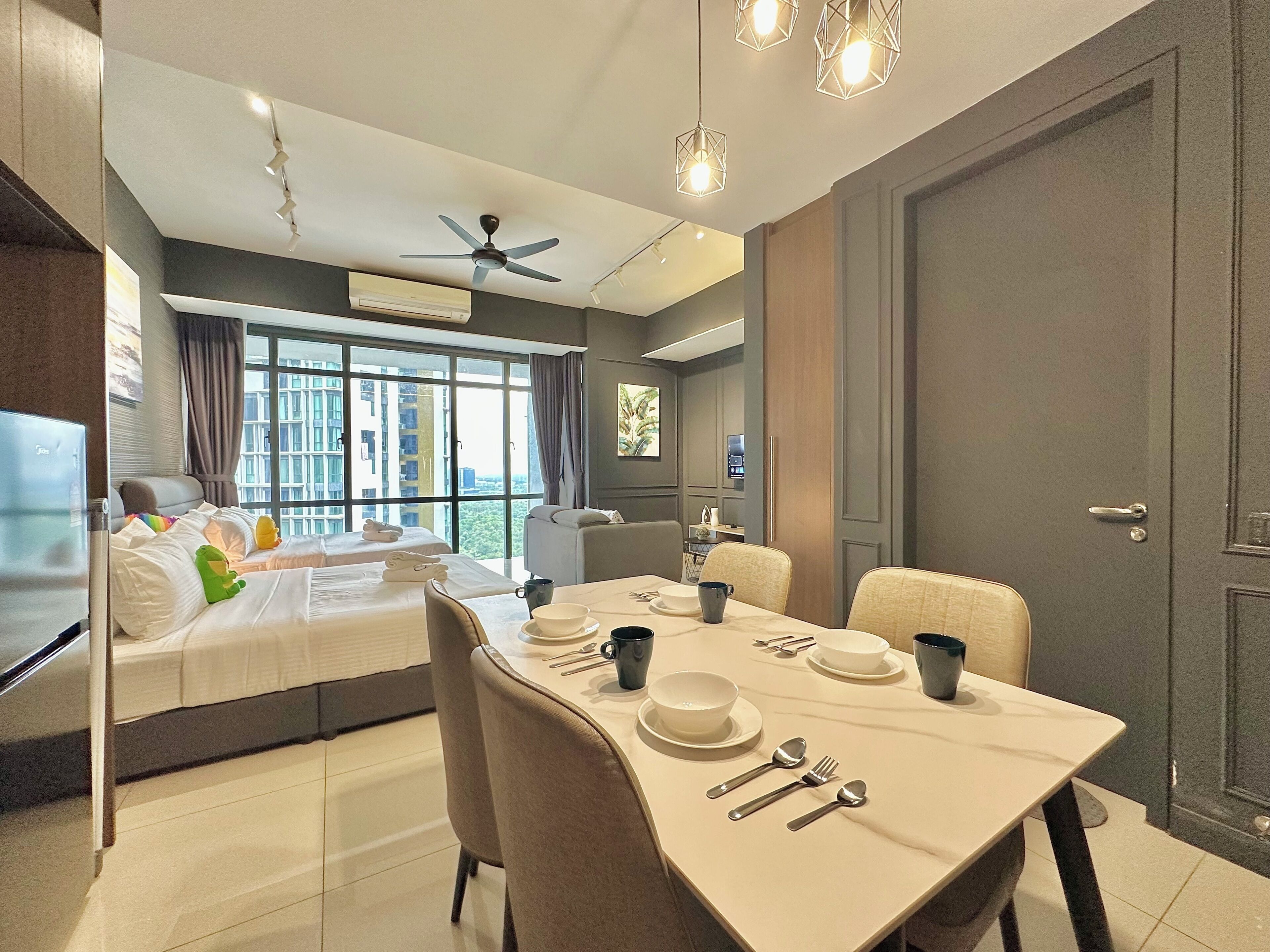 A hotel room with a dining area, a bed with towels, a ceiling fan, and a view of the city.
