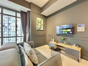 A modern living room with a sofa, a flat-screen TV, a console table, and a window with curtains. - Grand Medini Residence by Stayrene  (Iskandar Puteri)