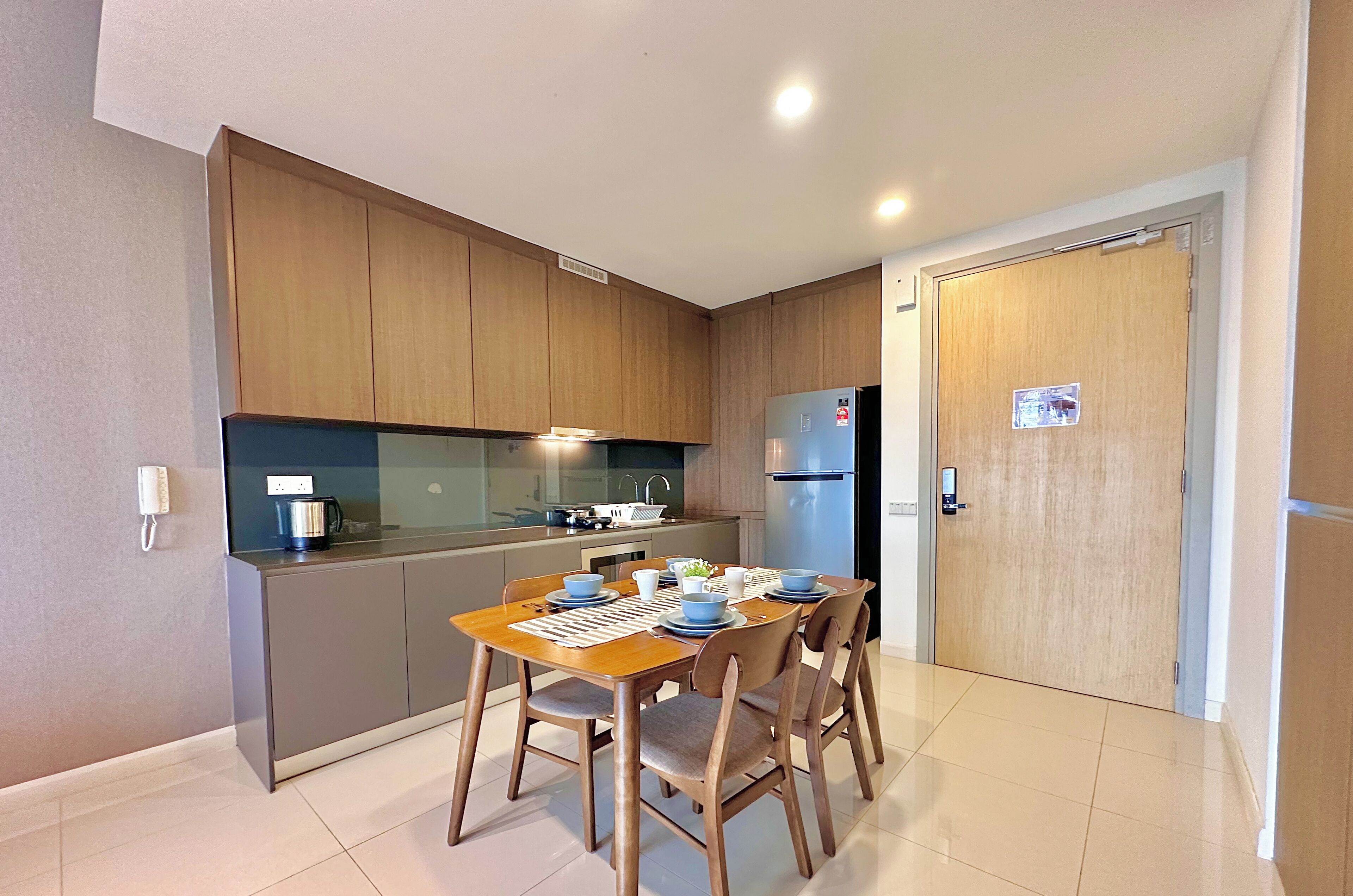 A modern kitchen with wooden cabinets, a stainless steel refrigerator, and a dining table set for four.