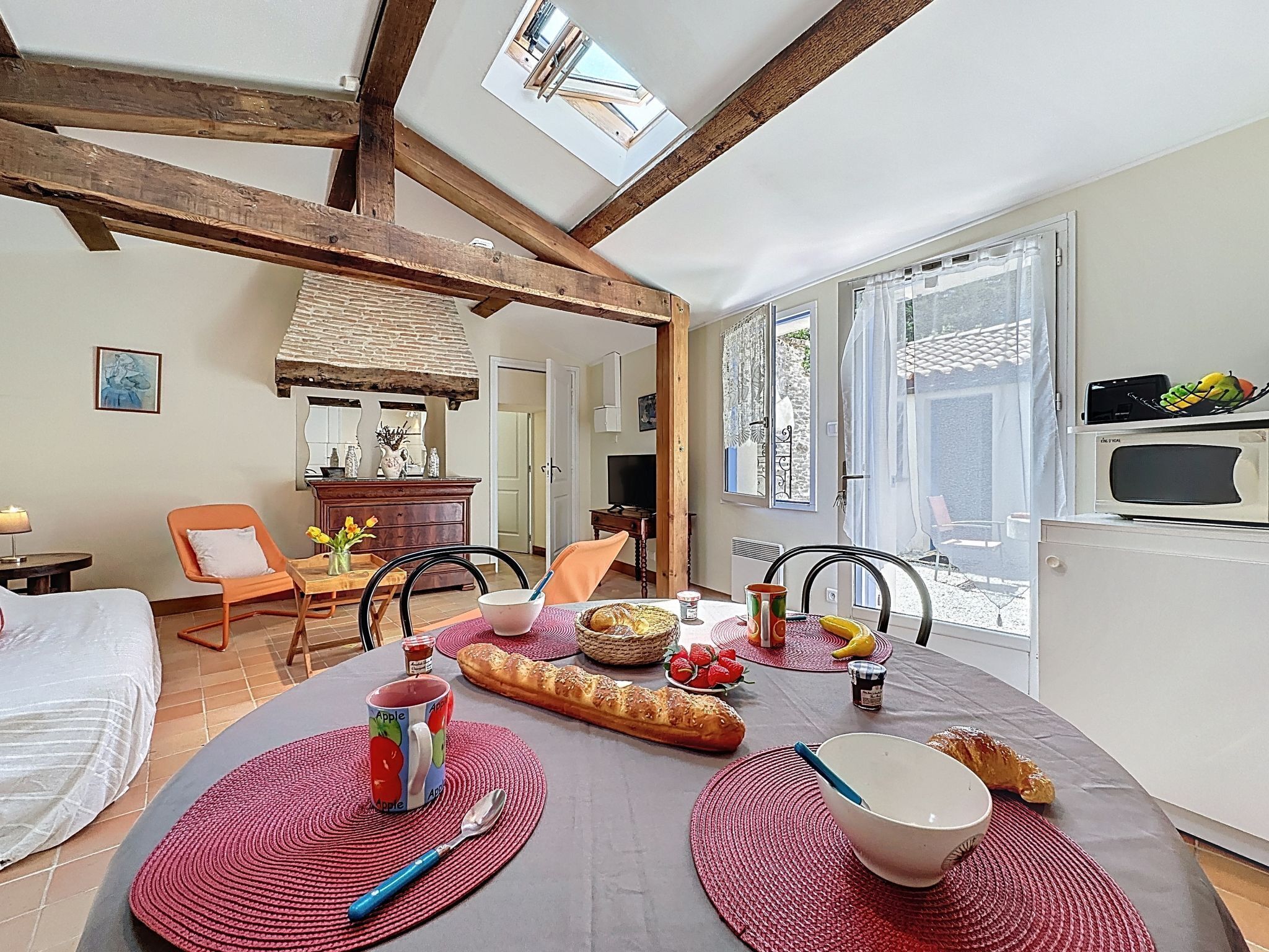 A cozy dining area with a table set for breakfast, featuring bread, fruit, and a mug.