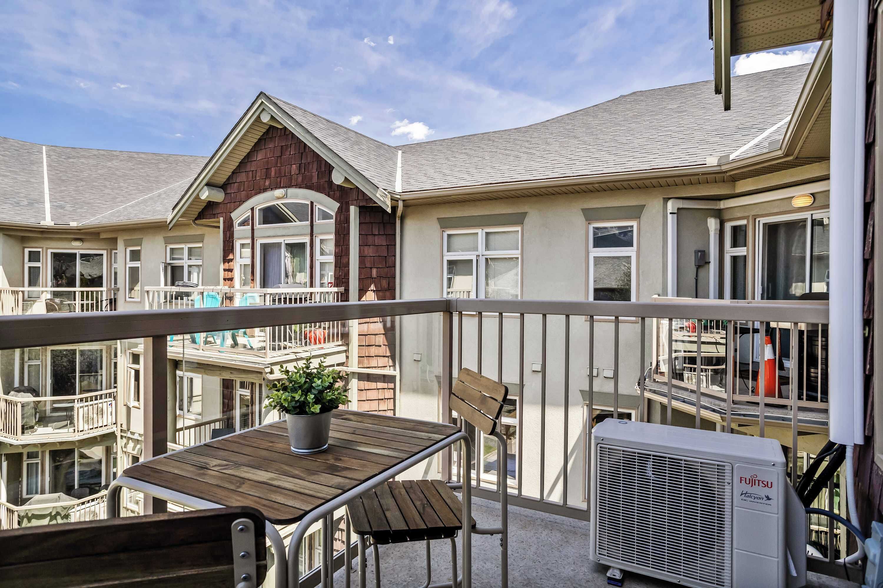 A balcony with a wooden table, a potted plant, and an air conditioning unit.