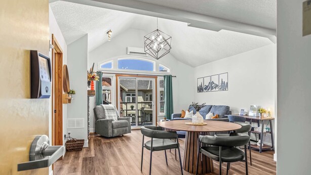 Een moderne woonkamer met een houten vloer, een ronde eettafel met vier stoelen, een grijze bank en een groot raam.