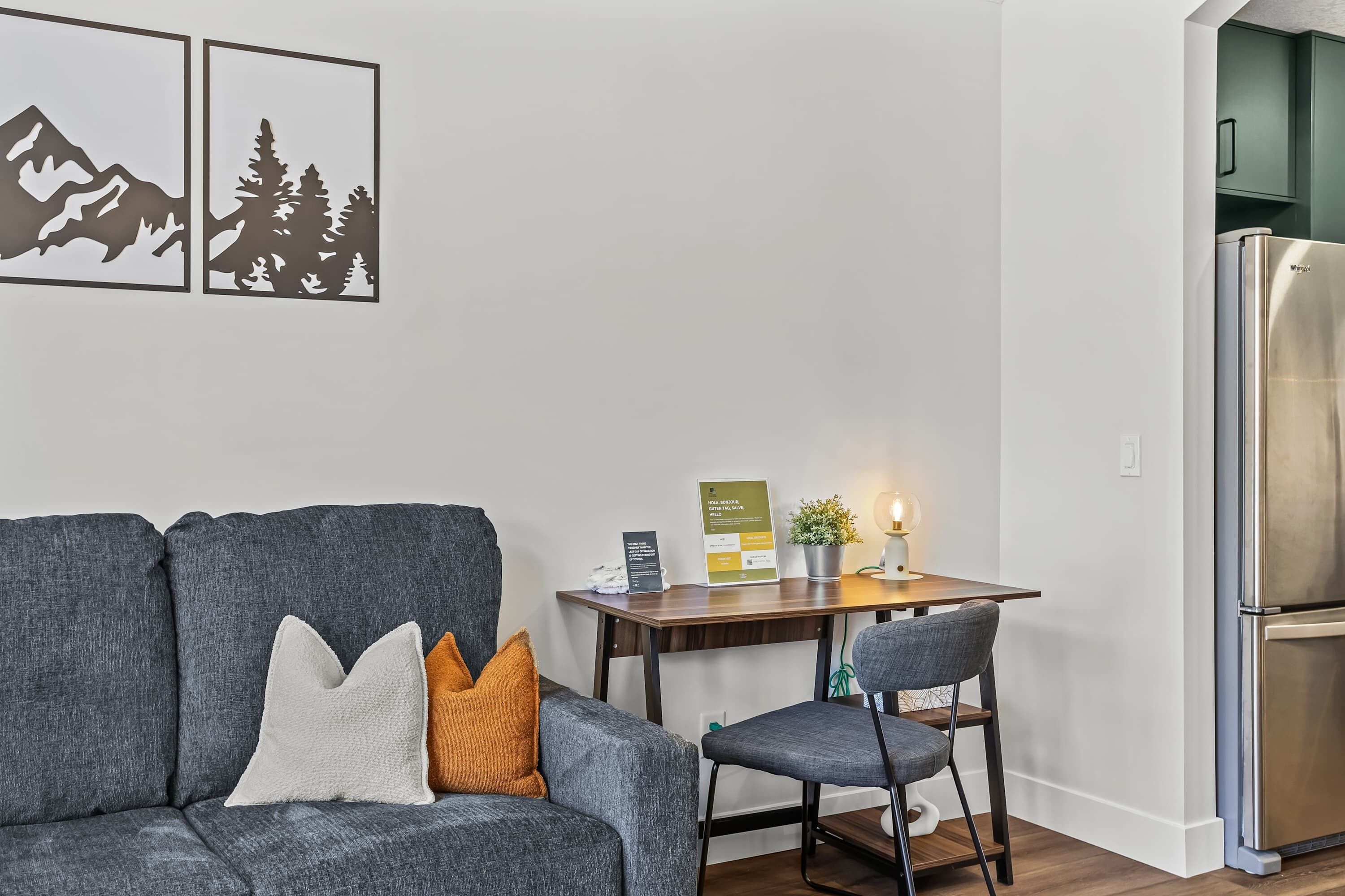 Un salon moderne avec un canapé gris, une table en bois et un réfrigérateur en acier inoxydable.