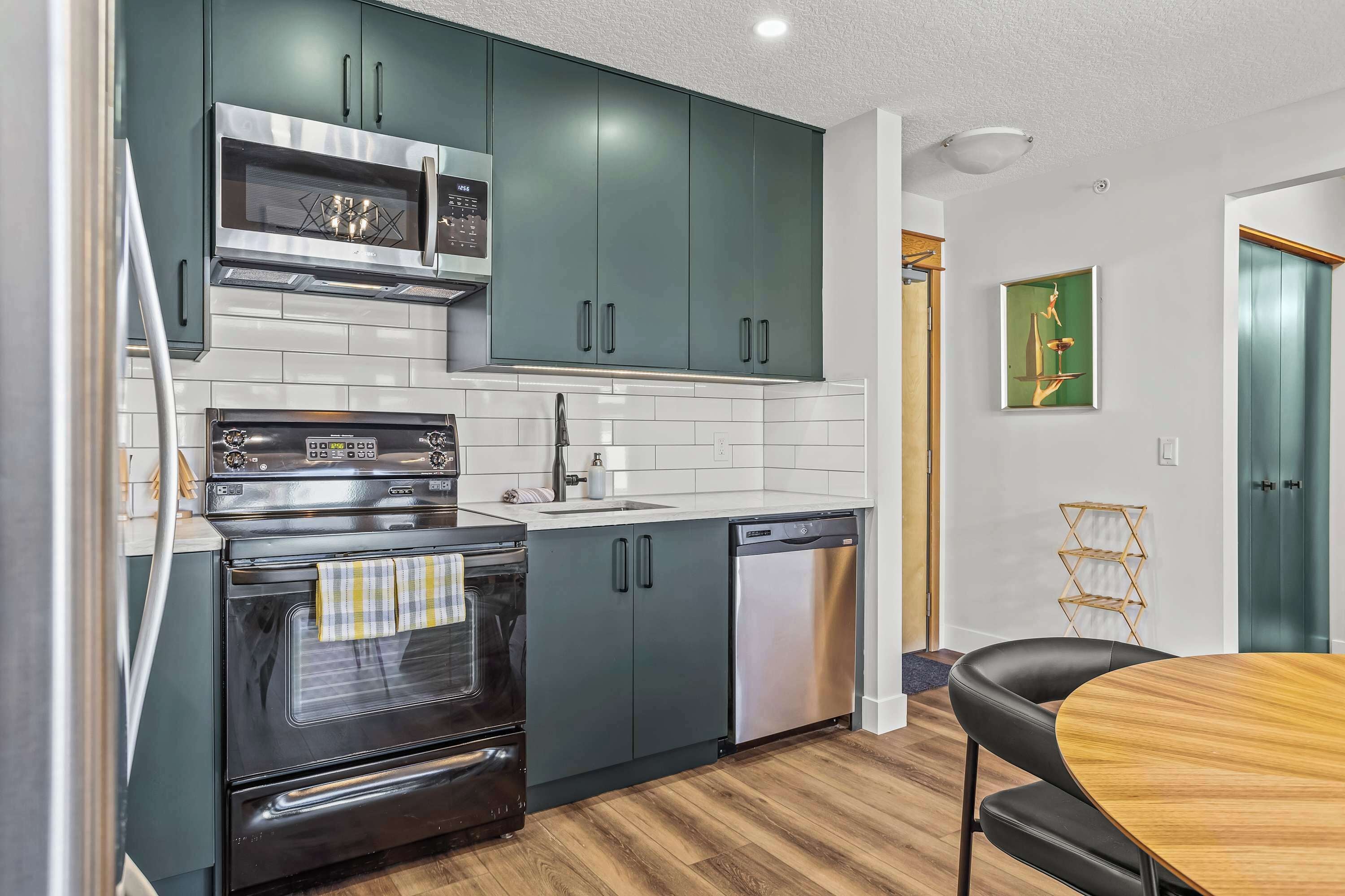 A modern kitchen with dark green cabinets, stainless steel appliances, and a wooden dining table.
