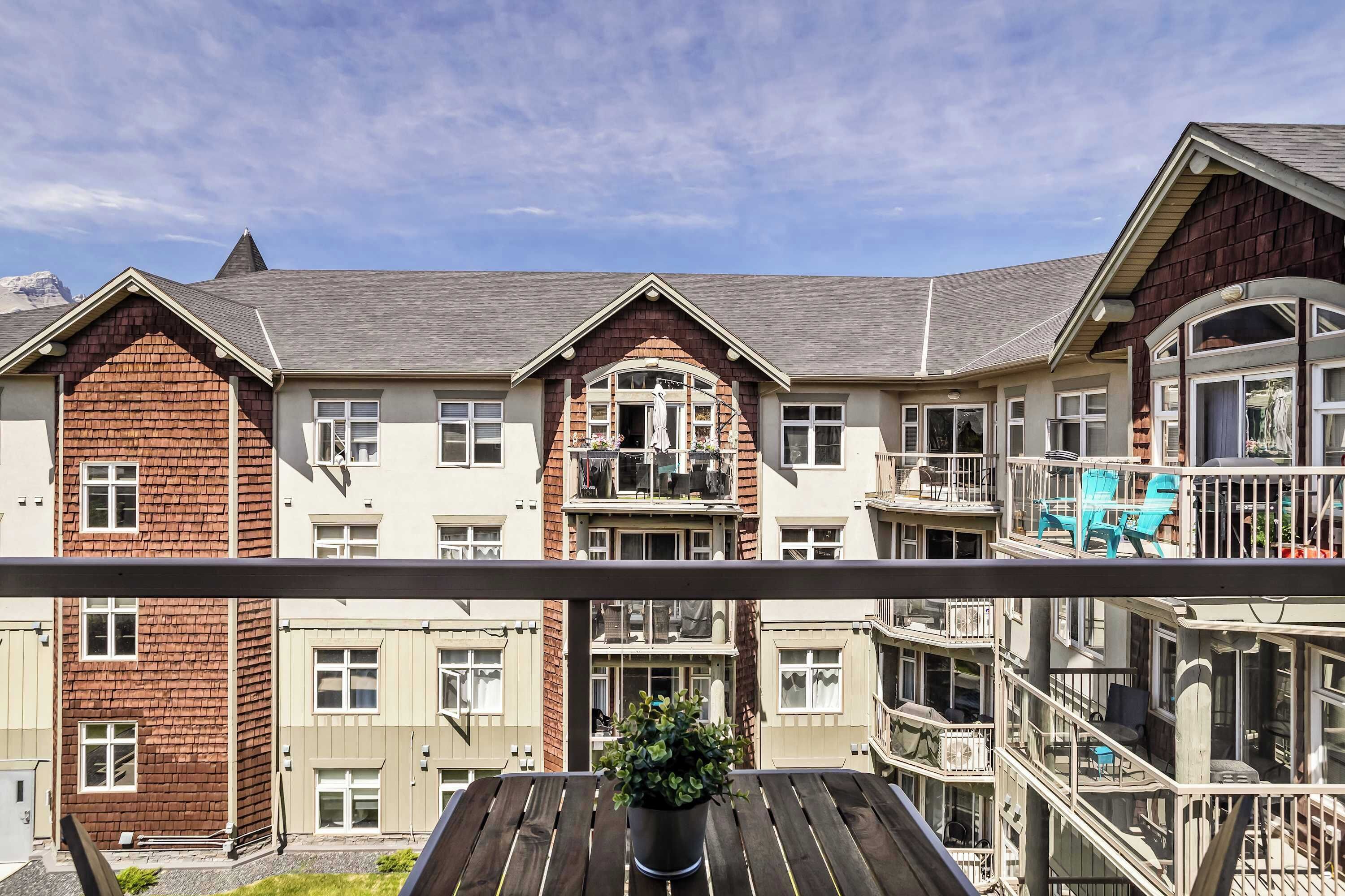 A multi-story residential building with balconies, a wooden deck, and a potted plant.
