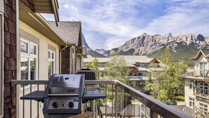 Een balkon met een barbecue, met uitzicht op een woongebied met huizen en bergen op de achtergrond.
