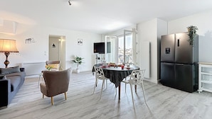 A modern living room with a sofa, a dining table with chairs, a TV, and a refrigerator. - Les Roches by Interhome (Pornic)