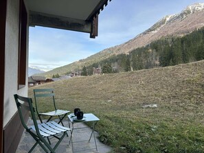A patio with a table and chairs, overlooking a mountainous landscape with houses in the distance. - Lauzière Dessus 22 - Crève Coeur (LES AVANCHERS VALMOREL)